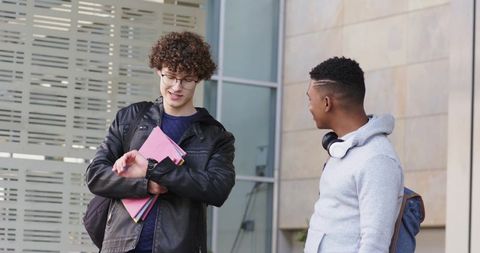 College students checking time and chatting outside modern campus building with backpacks and notebo