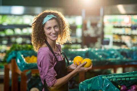 Smiling Grocery Worker Holding Fresh Oranges in Produce Section