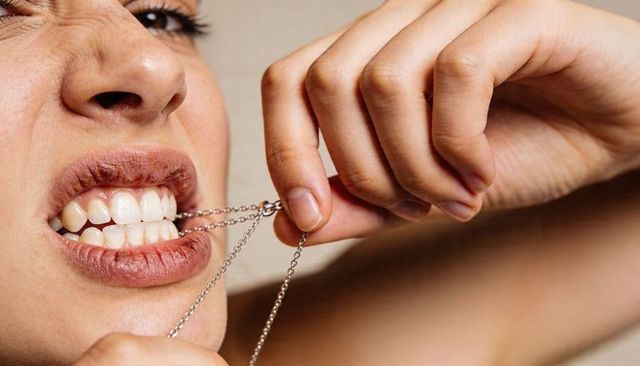 Close-up of woman biting silver necklace, teeth gripping chain, lips and hand tension
