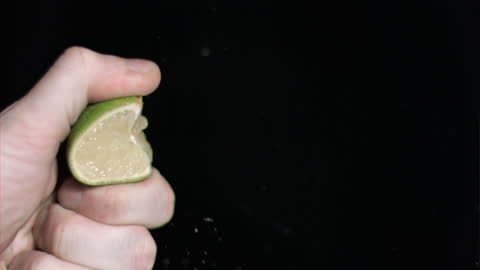 Hand Squeezing Lime Juice on Black Background