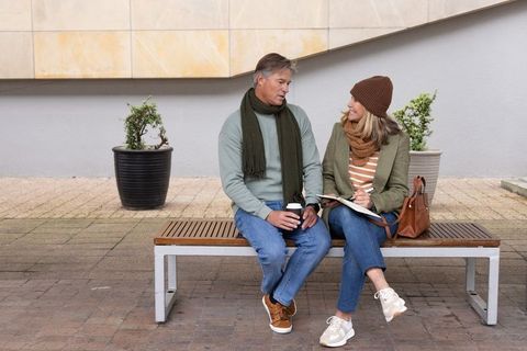 Middle-aged couple sharing coffee and notebook on urban bench, casual autumn conversation