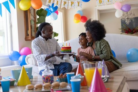 African american family throws birthday party for child with colorful rainbow cake and balloons