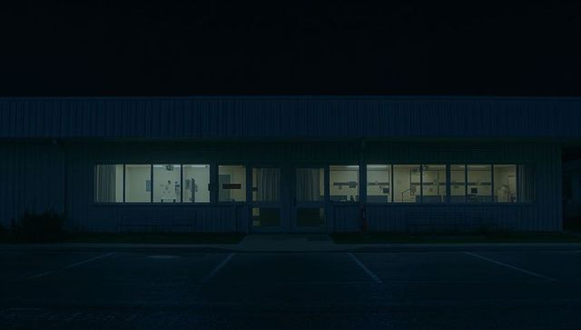 Nocturnal office exterior glowing through windows showing lit interior and parking bays