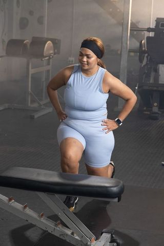 African american woman performing lunge at gym wearing light blue active set and headband