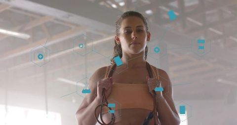 Standing woman holding jump rope with AR health icons overlay in backlit industrial gym