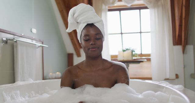 Happy african american attractive woman relaxing in foam bath in bathroom. beauty, pampering, home spa and wellbeing concept.