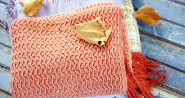 Comfortable knitted blankets with dry autumn leaves lying on wooden floor. Perfect for themes involving autumn, coziness, interior design, and seasonal decor. Can be used for promoting autumn sales or as a background for fall-themed content.