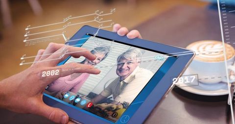 Tapping tablet for video call with smiling seniors at cafe with holographic timeline app