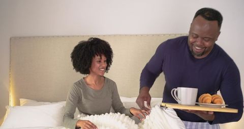 African American couple sharing cozy breakfast in bed with tray, coffee and croissants