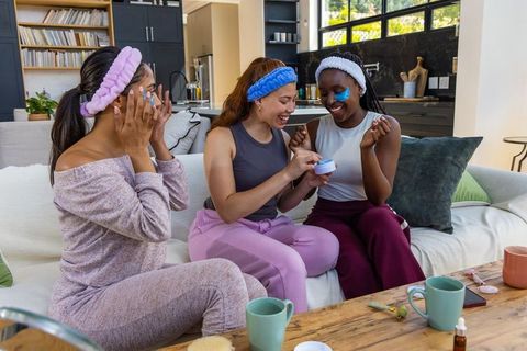 Multicultural friends enjoying at-home spa night applying eye patches and face cream