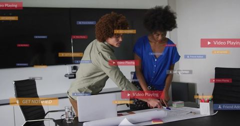 Colleagues collaborating over blueprint with floating digital notifications in office