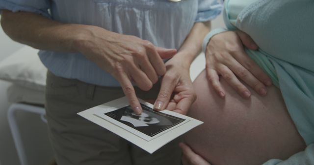 Doctor pointing at ultrasound result while pregnant woman listens. Ideal for content about maternity healthcare, pregnancy journey, medical consultations, prenatal care, and parenthood.