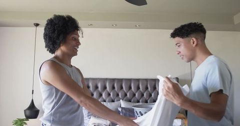 Young men folding laundry together in bright bedroom showing teamwork and home life