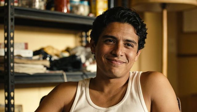 Hispanic man smiling and relaxing in cluttered home workspace with metal shelving