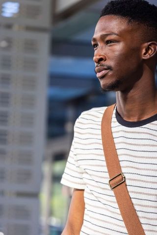 African american man gazing thoughtfully on urban transit platform with crossbody bag