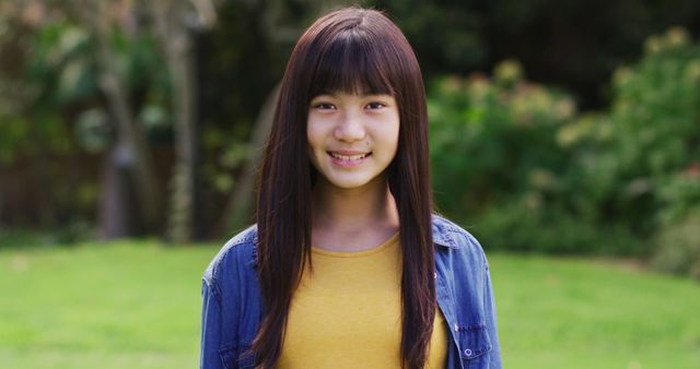 Young Asian girl standing outdoors with a smile, wearing casual clothes. Ideal for use in campaigns promoting outdoor activities for youth, teenage life, or casual fashion. Suitable for educational materials, social media content, or multicultural family themes.