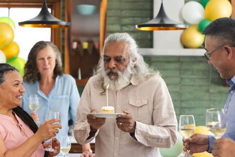 Senior man celebrating birthday with cupcake candle surrounded by diverse friends