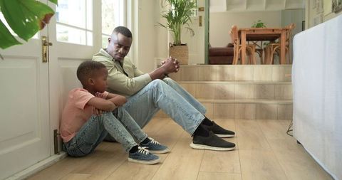 African american father and son sharing quiet conversation on sunlit entryway floor