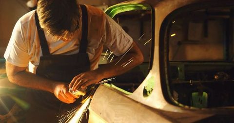 Auto body repair: technician restoring carframe with angle grinder