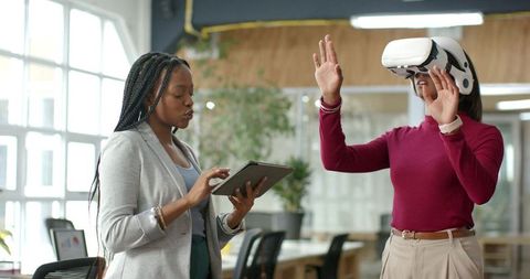 Diverse coworkers collaborating while guiding vr user with tablet in modern office