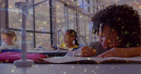 Elementary students writing and reading in sunlit classroom with study lamps