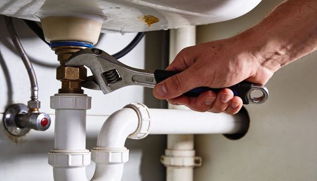 Tightening wrench on brass coupling under sink, closeup of hand and plumbing repair for maintenance