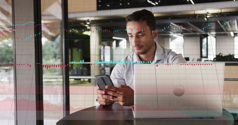 Professional checking trading app on smartphone while analyzing market charts on laptop in cafe