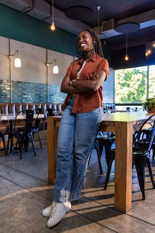 African american woman leaning on communal table in modern cafe wearing lavalier mic