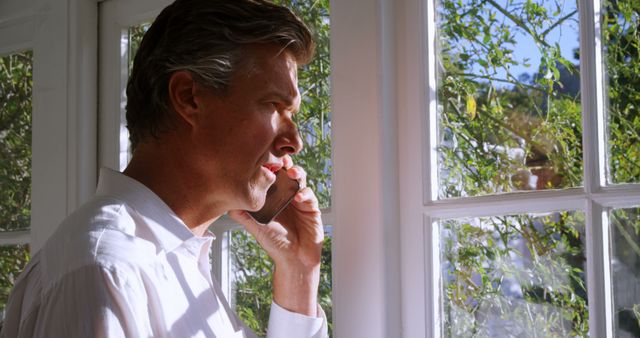 Mature Man Talking on Smartphone by Window with Natural Light - Download Free Stock Images Pikwizard.com