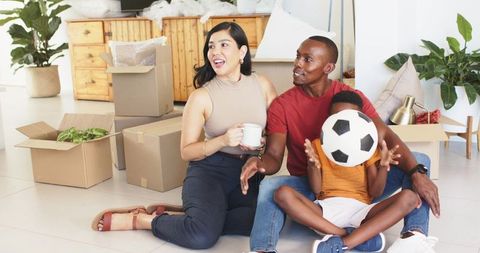 Happy family unpacking new home sitting on floor with child playing with soccer ball