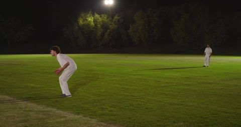 Night cricket fielders crouching and standing under floodlights on green outfield