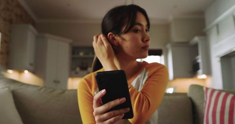 Asian Woman with Smartphone Relaxing on Beige Sofa