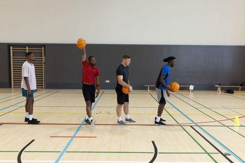 Diverse male basketball players practicing dribbling and passing drills on indoor court