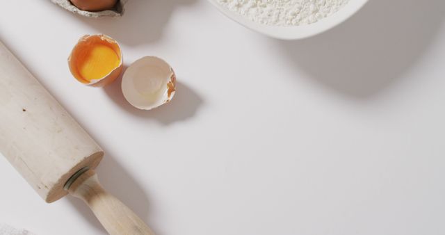 Top view of baking ingredients including egg shells and flour along with a rolling pin. Suitable for use in articles, blogs, or advertisements related to cooking, baking recipes, food preparation, bakery shops, or culinary tutorials.