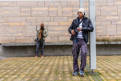 Diverse male commuters leaning and listening to music while checking phone at urban plaza