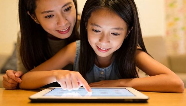 Preteen girl learning on tablet while mother watching, bonding through digital learning