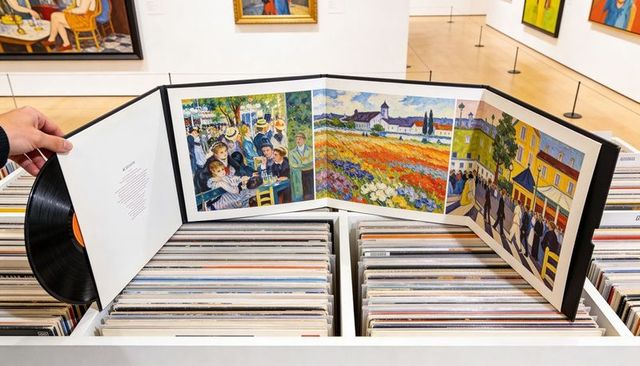 Browsing vinyl collection holding trifold album displaying impressionist prints in gallery