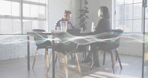 Young professionals discussing strategy at modern bright office table with digital waveform overlay