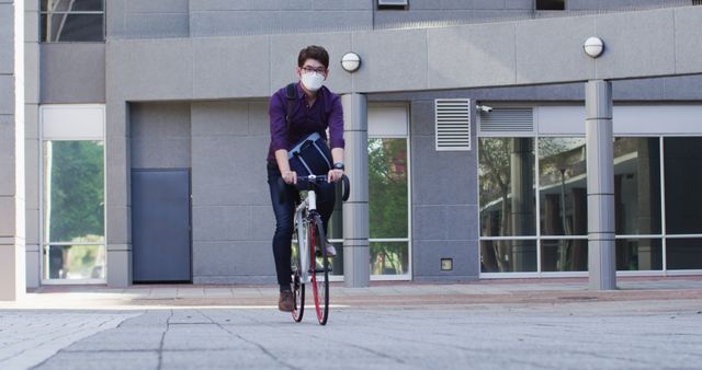 Office employee cycling to work in urban setting, wearing formal attire and a protective mask. Useful for themes related to sustainable commuting, urban lifestyle, health precautions, and work-life balance.
