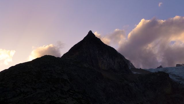 This visually striking silhouette of a mountain peak at sunset, accompanied by dramatic clouds, is perfect for nature, adventure, and travel websites, printed wall art, and promotional materials for outdoor activities or tours. The image captures the subtleties of twilight and the rugged beauty of highlands, ideal for emphasizing natural beauty and adventure themes.