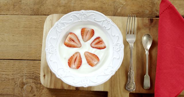 Slices of strawberries in plate with spoon on chopping board