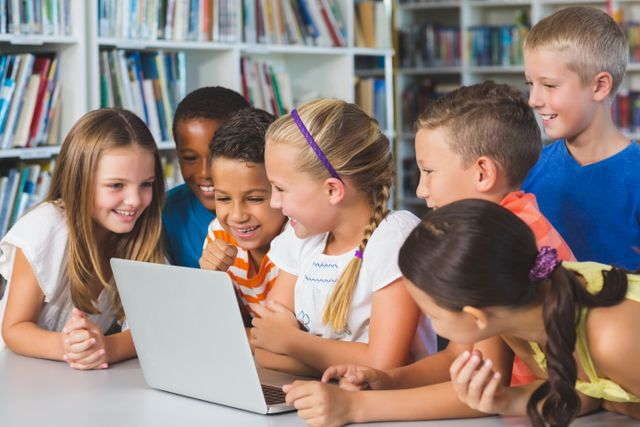 Kids gathered around a laptop in a library, excitedly learning together. Ideal for educational websites, technology in education promotions, children's books, or team-building activities. Captures teamwork and curiosity in an academic setting.