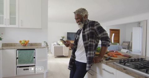 Man in Plaid Shirt Browsing Smartphone Beside Cutting Board in Modern Kitchen