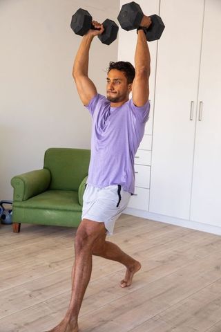 Man executing overhead lunge with dumbbells in minimalistic home gym