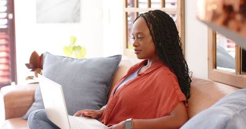 African woman working remotely on laptop from cozy living room wearing smartwatch at home