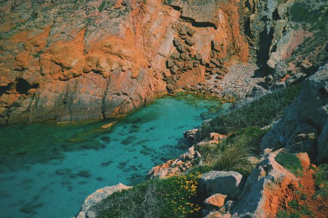 Turquoise water contrasts with rugged red rock cliff, creating a stunning natural view. Ideal for travel blogs, nature photo collections, environmental talks, and promotional materials for hiking or coastal destinations.