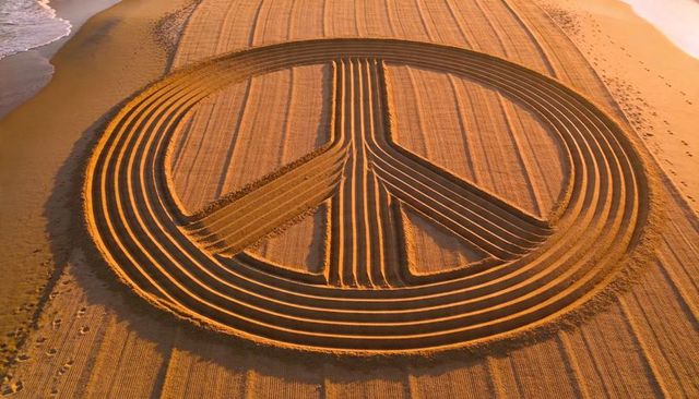 Aerial golden-hour peace symbol sand sculpture carving with concentric grooves on beach