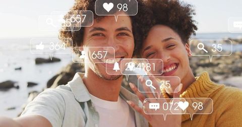 Young couple taking selfie at rocky seaside with social media notification overlays