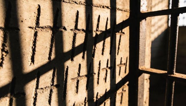 Sunlit concrete wall with hand-carved cross marks and barred shadow pattern