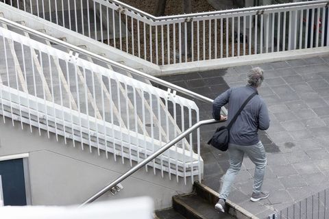 Senior man ascending concrete urban stairs holding metal handrail and crossbody bag